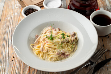 Carbonara creamy pasta with bacon crisps on a light wooden table in a restaurant