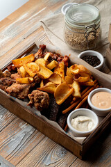 Beer snacks in a wooden tray: french fries, baked potato and chicken wings with sauces