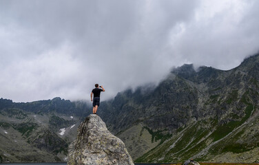 Man standing on big boulder with smartphone and taking photo mountain peaks and lake at High Tatras, Slovakia