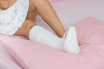 Leg in plaster of a teenage girl on a pink bed after an accidental fall with an ankle fracture.Fracture of the lower leg in a child
