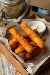 Deep fried cheese sticks laid in grid with tzatziki sauce in a wooden table, close up of beer snacks