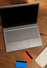 laptop with black screen orange credit cards and notepad on wooden table