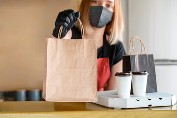 Food bag, pizza, drink package to go in takeaway restaurant. Kitchen worker issues online orders in gloves and mask. Takeaway food paper bag mock up. Contactless food delivery lockdown covid 19.