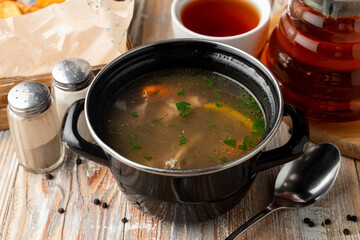 Spicy and warm autumn soup on meat broth, served in rustic pot on a wooden table