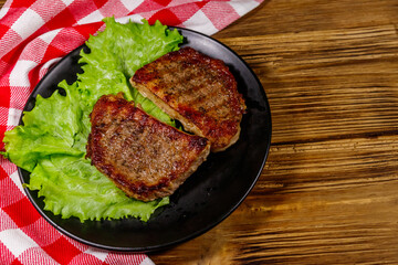 Grilled pork steaks with lettuce leaves on wooden table. Top view