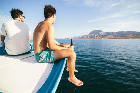 View of two men friends enjoying a beer and traveling on a boat through scenic view of sea and mountains