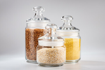 Jars with buckwheat couscous and barley on a white background