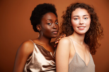 Obraz premium two pretty girls african and caucasian blond posing cheerful together on brown background, ethnicity diverse lifestyle people concept