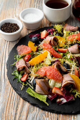 Fototapeta na wymiar Roast beef salad with lettuce and orange segments on a black stone dish