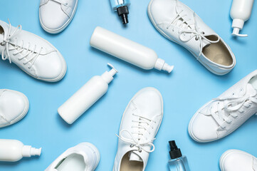 White leather sneakers, plastic bottles of cleaning products for shoes on blue background flat lay...