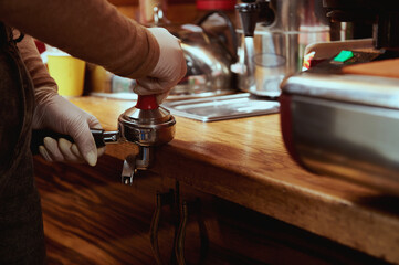 Closeup of female barista's hands tempering, pressing ground coffee in metal portafilter. Tamping coffee