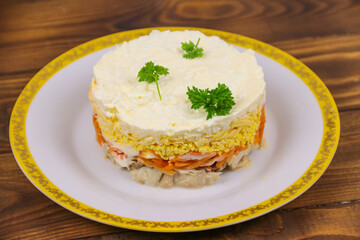 Tasty layered salad with chicken, carrot, eggs, cheese and mayonnaise on wooden table