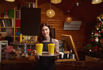 Barista holds a tray with yellow takeaway paper cups of coffee and showing it at camera