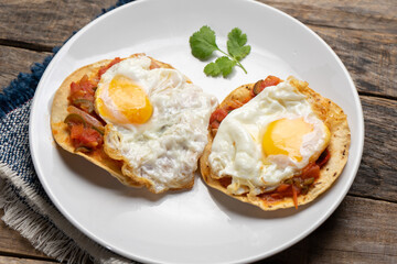 Fried eggs with sauce and tortilla called rancheros for  breakfast on wooden background. Mexican food