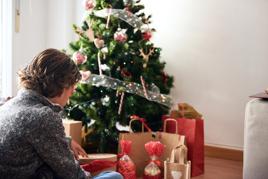 Kid with curly hair sitting at Christmas tree