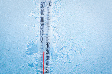 Frosty winter window with ice patterns and a thermometer showing a minus temperature