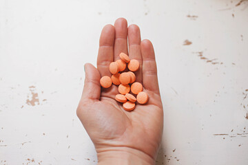 Hand holding Vitamin C tablets against white table top