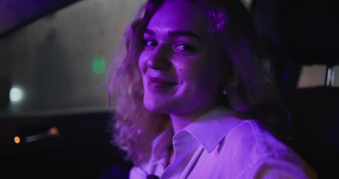 Sexy and shy woman grimacing flirting sitting in a car at night, violet light
