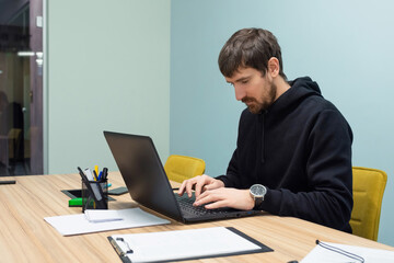 Young man working on a laptop sitting at his workplace in the office. Consulting, training, co-working, business concept