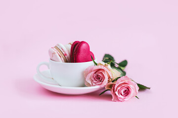 Tasty french macaroons with pink roses in a white cup. Heart-shaped macaron.