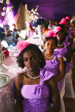 Bridesmaids In Pink Hats Sit At A Table During A Wedding In Nigeria.