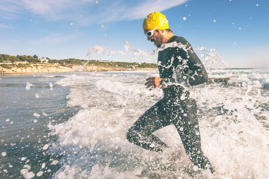 Triathlete running in to the water on triathlon race. Splashing water.