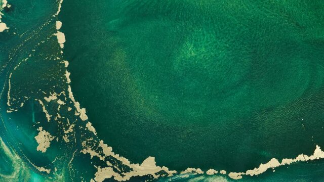 Green-gold background of fluid art close-up, with space for text. Abstract aqua ocean waves ink texture. Green tide watercolor paint backdrop. Turquoise liquid and gold glitter spreads by sea waves