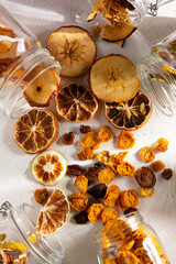top view of dried fruit, apple, lemon, tangerine, grapes, golden berries and glass jars on a white background
