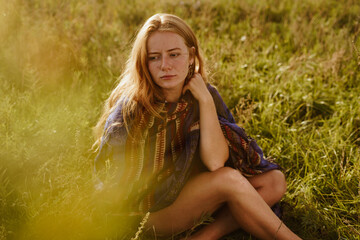 thoughtful look, sadly closed lips and slightly shifted eyebrows on the face of a red-haired beauty without makeup with an ethno cape on her shoulders not covering the beautiful strong and slender