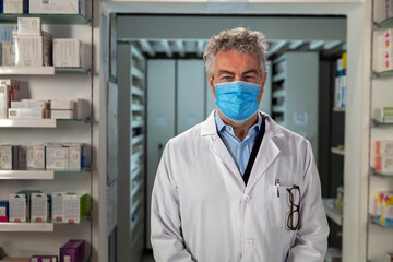 Fototapeta na wymiar Cinematic shot of male pharmacist consultant with protective medical mask is smiling satisfied with his job in camera in pharmacy. Concept of covid-19, protection, coronavirus, safety, health care.
