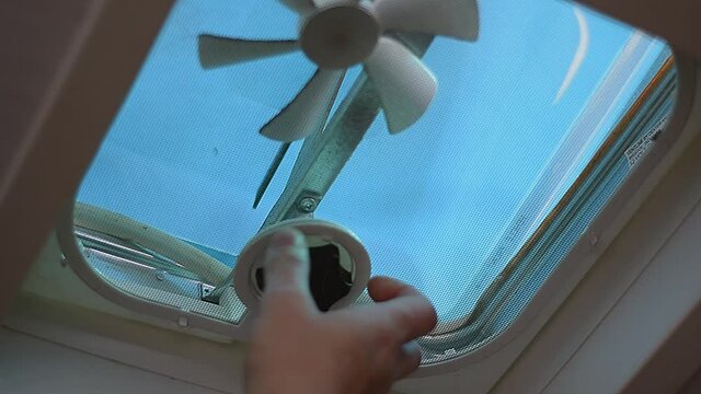 Man opening roof ventilation fan by manually cranking turning knob to let out heat humid hot air in camper van travel trailer motor home.