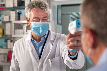 Cinematic shot of male pharmacist with medical mask is measuring temperature with infrared...