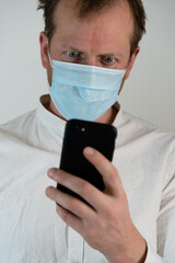 Portrait of a straight man with a white shirt with curly hair and a direct firm look and face mask to protect against covid19, he has a black mobile phone