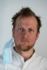 Obraz premium Close up portrait of a man with a smile on his face and a covid 19 protective mask on one side of his head looking straight down
