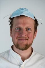 Close up portrait of a man with a smile on his face and a covid 19 protective mask on his head looking straight down