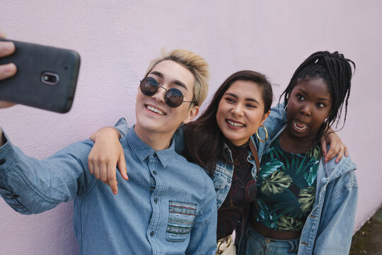 Friends taking selfie together on pink wall