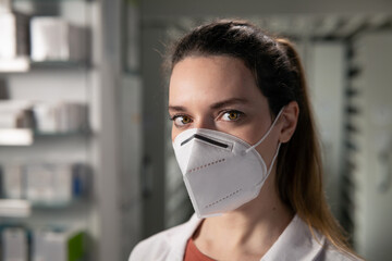 Cinematic macro shot of female pharmacist consultant with protective N95 respirator mask is looking in camera in pharmacy. Concept of covid-19, protection, coronavirus,prevention, safety, health care.