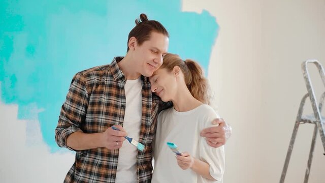 Young couple hugging and stains each other's noses brushes with blue paint during apartment renovation