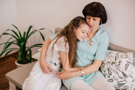Mother and daughter sitting at sofa and hug each other