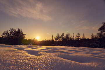 Snow in the foreground on a frosty winter evening at sunset as a backdrop and blurred forest on the...