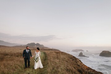 A Bride and Groom Walking on a Cliff by the Ocean