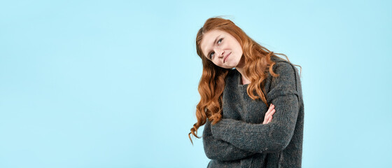 A young pretty girl in a knitted sweater shows emotions on a light blue background. A place to copy...