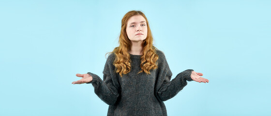 A young pretty girl in a knitted sweater shows emotions on a light blue background. A place to copy...