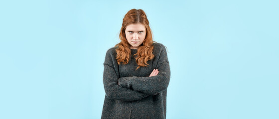A young pretty girl in a knitted sweater shows the emotion of resentment on a light blue...