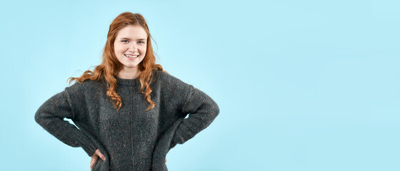 A young pretty girl in a knitted sweater shows emotions on a light blue background. A place to copy...