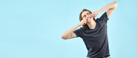 Portrait of an emotional friendly young man in a T-shirt fooling around on camera on an isolated blue background