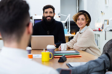 Businesspeople smiling at their colleague sitting against them at desk.
