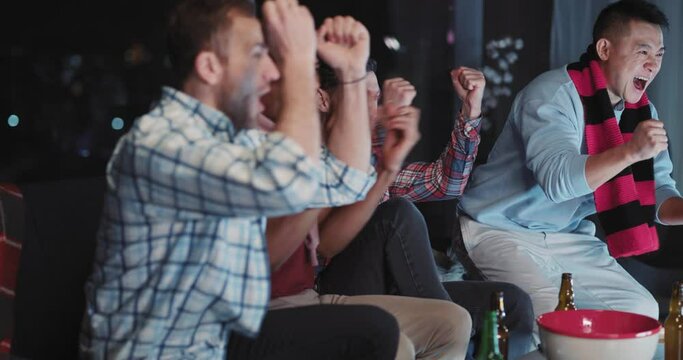 Side view of happy successful multi-ethnic friends celebrating football victory game watching on TV doing high-five together.