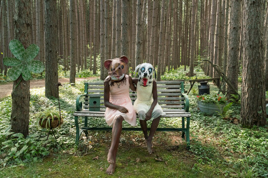 Two black girls wearing a dog and squirrel mask sitting on a ben