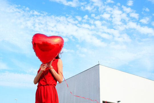 Anonymous female model with red heart ballon outside on a sunny day